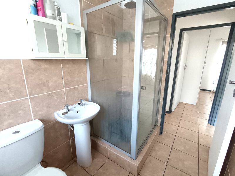A functional bathroom featuring a pedestal basin, toilet, and a glass-enclosed shower with neutral wall and floor tiling.