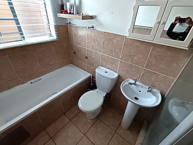 A functional bathroom featuring a bathtub, pedestal basin, and toilet with neutral wall and floor tiling, offering a practical layout for renovation.