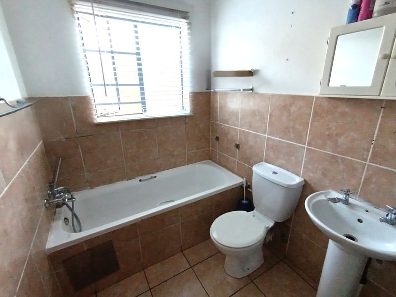 A dated bathroom featuring a bathtub, pedestal basin, and toilet with tiled walls and flooring, requiring cosmetic updates and repairs to wall finishes.