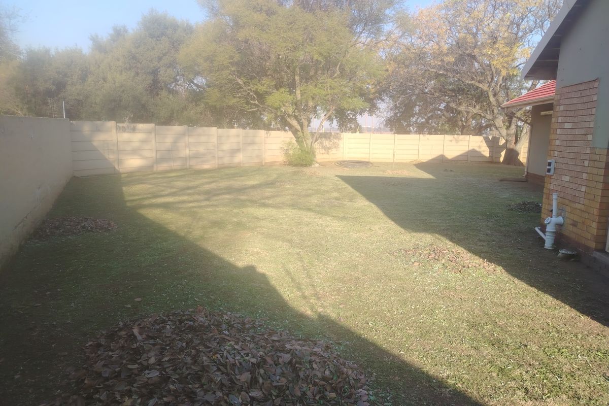 A spacious rear garden featuring a large lawn area enclosed by a precast concrete boundary wall and adjacent to the brick house exterior.