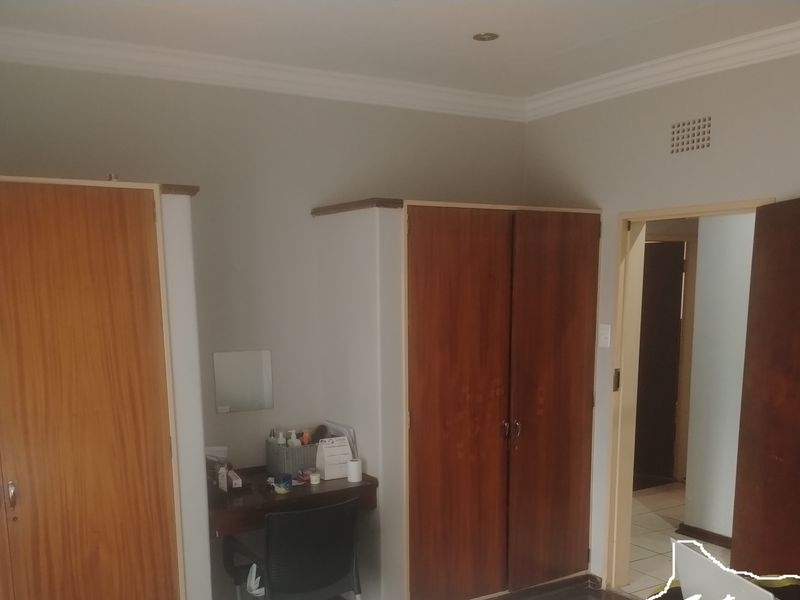 A bedroom featuring built-in wooden cupboards, crown molding, and recessed ceiling lighting, providing functional storage and a neutral aesthetic.