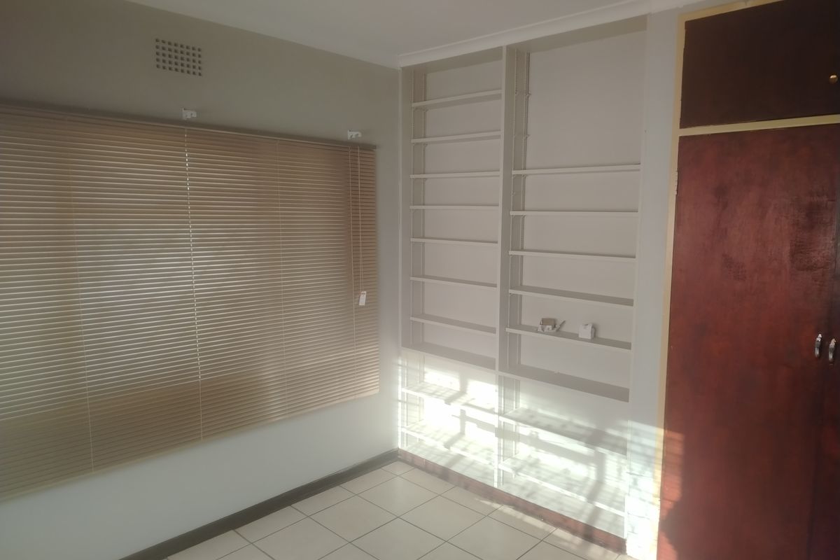 A bright, empty bedroom featuring tiled flooring, built-in shelving units, and venetian blinds, offering a clean canvas for personalization.