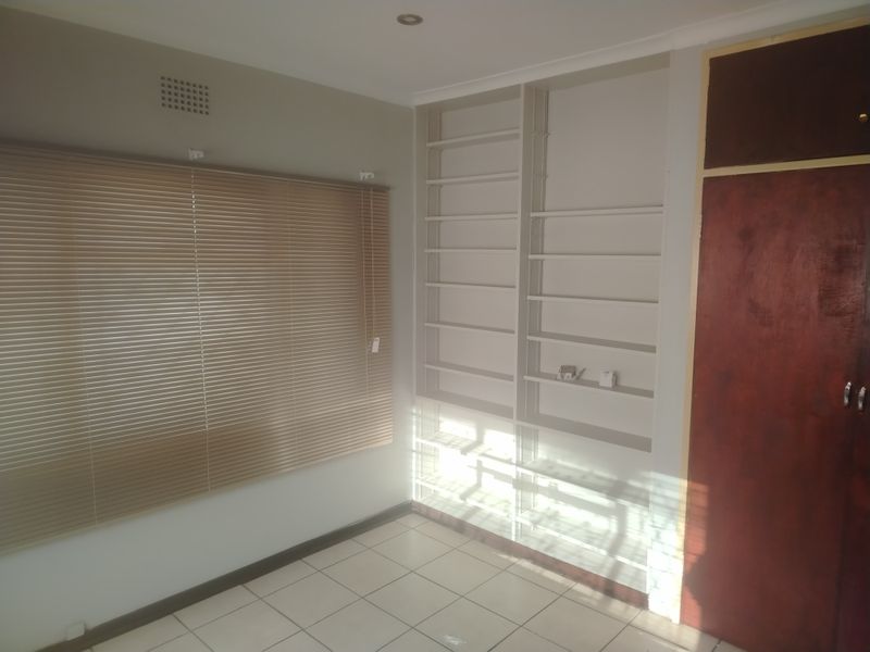 A bright, empty bedroom featuring tiled flooring, built-in shelving units, and venetian blinds, offering a clean canvas for personalization.