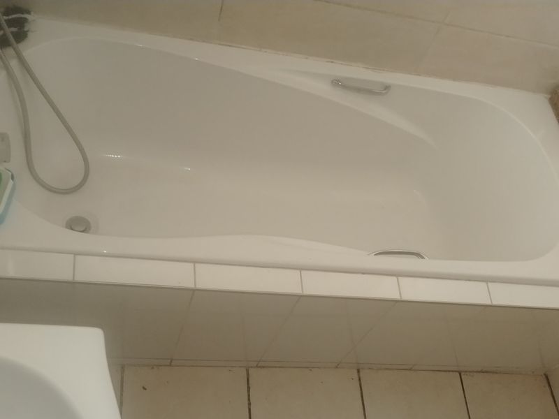A functional bathroom featuring a built-in bathtub with a shower mixer, complemented by neutral ceramic wall and floor tiles with a decorative mosaic inlay.