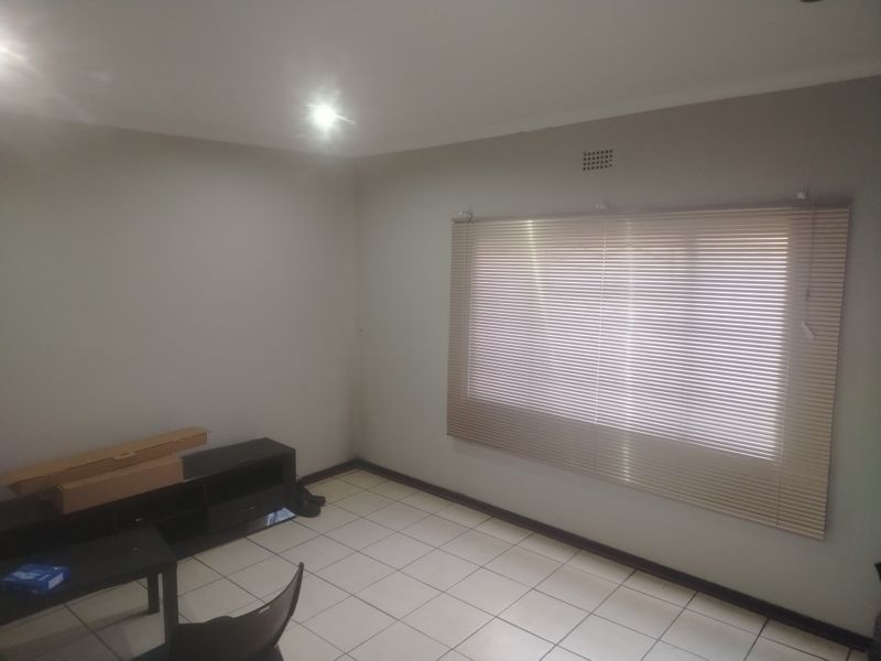 A neutral, tiled living area featuring recessed downlights and venetian blinds, offering a clean and versatile space ready for personalization.