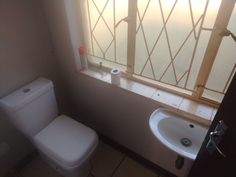 A compact bathroom featuring a white toilet and a wall-mounted basin, with security bars on the window.