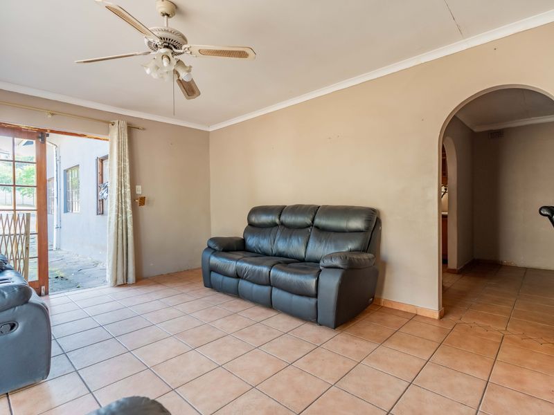 A living room featuring tiled flooring, a ceiling fan, and an arched entryway leading to other areas, with direct access to an outdoor patio.