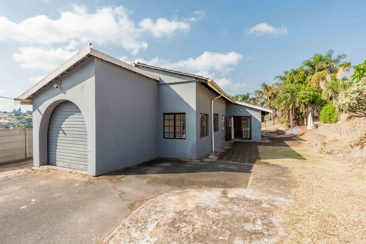 Rear exterior view of the property featuring a roller shutter garage door, paved driveway, and established garden area.