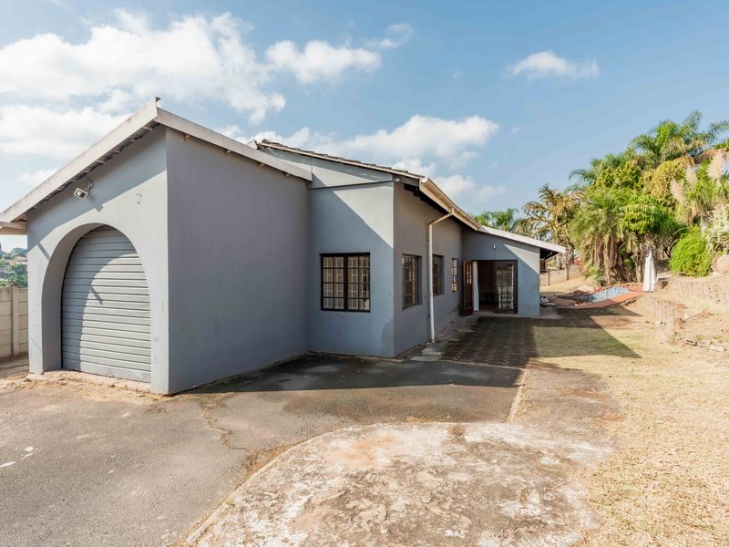 Rear exterior view of the property featuring a roller shutter garage door, paved driveway, and established garden area.