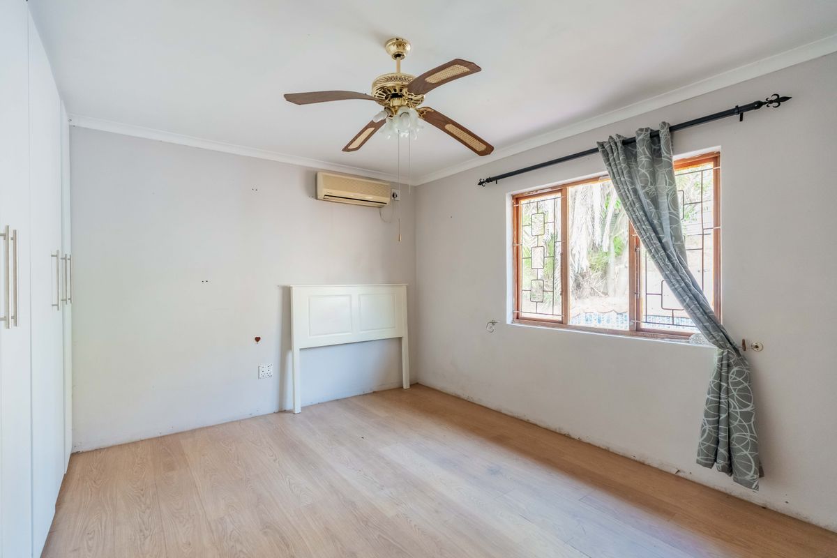 An empty bedroom featuring laminate flooring, a ceiling fan, split-system air conditioning, and built-in cupboards, requiring minor cosmetic repairs to walls and skirting.