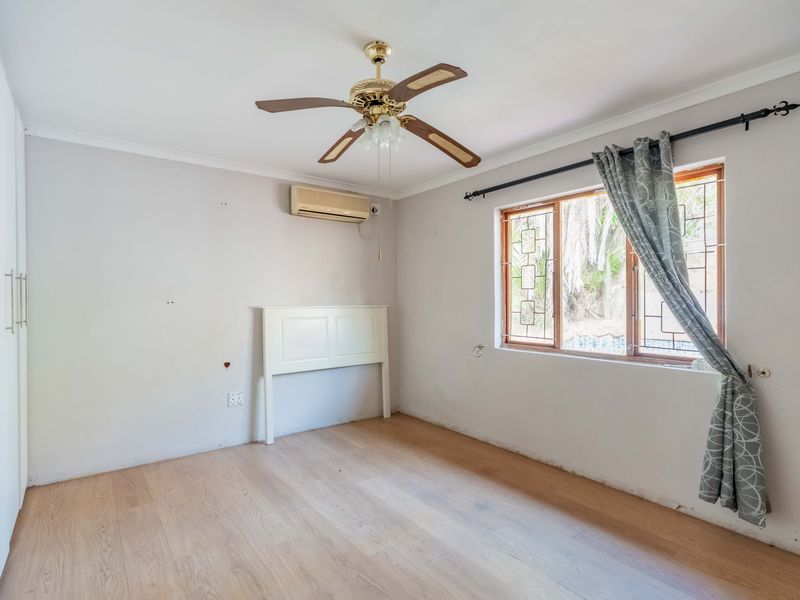 An empty bedroom featuring laminate flooring, a ceiling fan, split-system air conditioning, and built-in cupboards, requiring minor cosmetic repairs to walls and skirting.