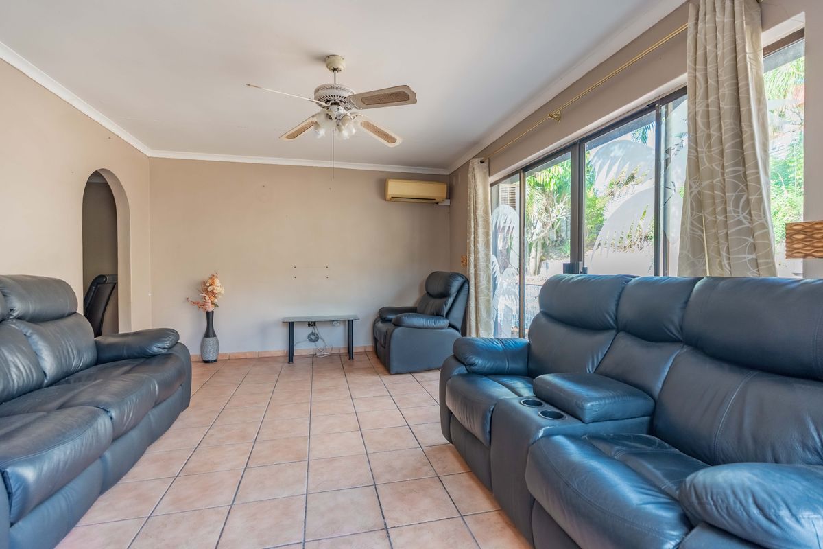 A living room featuring tiled flooring, a ceiling fan, wall-mounted air conditioning, and large sliding glass doors providing access to the exterior.
