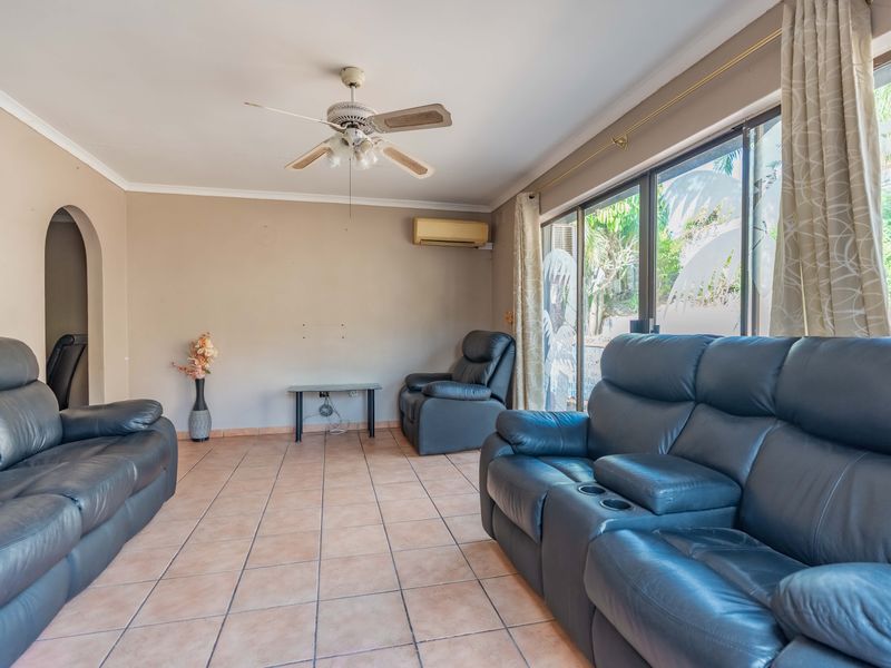 A living room featuring tiled flooring, a ceiling fan, wall-mounted air conditioning, and large sliding glass doors providing access to the exterior.