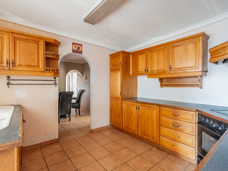 A functional kitchen featuring wooden cabinetry, laminate countertops, built-in oven, and ceramic hob, with an arched doorway leading to the adjacent living area.