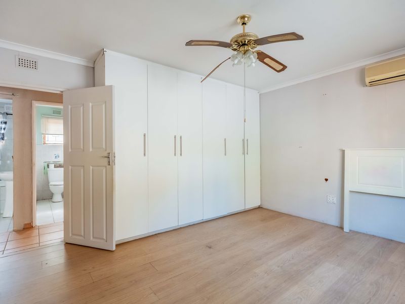 A spacious bedroom featuring built-in cupboards, a ceiling fan, and a split-system air conditioner, with direct access to an en-suite bathroom.