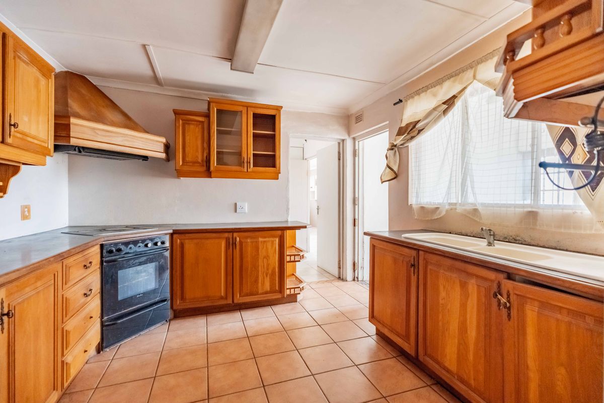 A dated kitchen featuring wooden cabinetry, a built-in oven with extractor fan, and tiled flooring, offering significant potential for modern renovation.