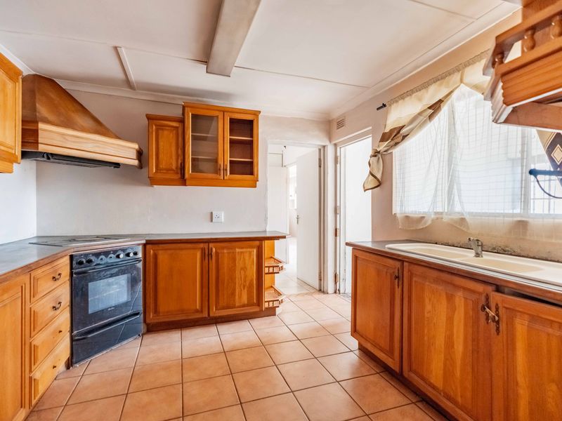 A dated kitchen featuring wooden cabinetry, a built-in oven with extractor fan, and tiled flooring, offering significant potential for modern renovation.