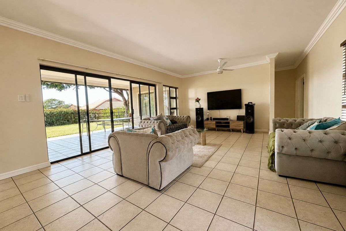 Spacious living room featuring neutral tiled flooring, decorative cornicing, and large sliding glass doors providing seamless access to the outdoor patio area.