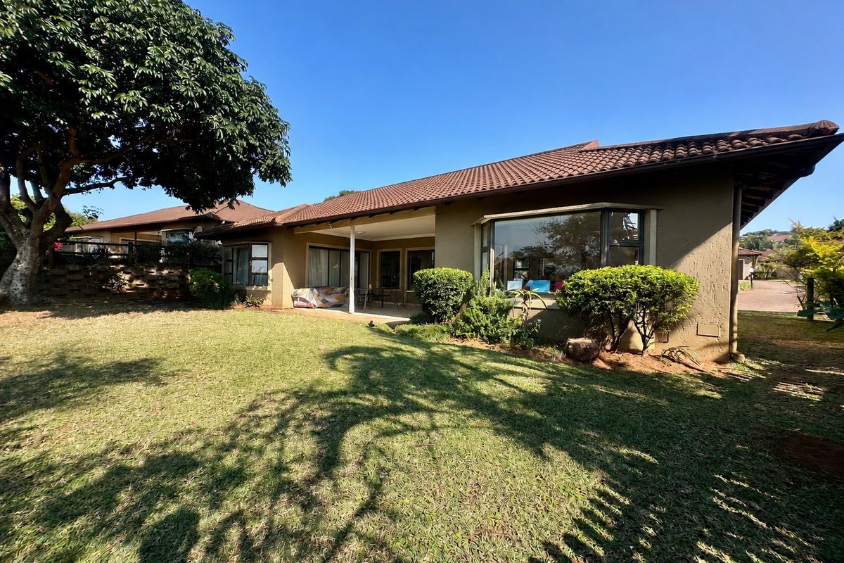 Rear view of the townhouse featuring a covered patio, large bay window, and a well-maintained garden area under a tiled roof.