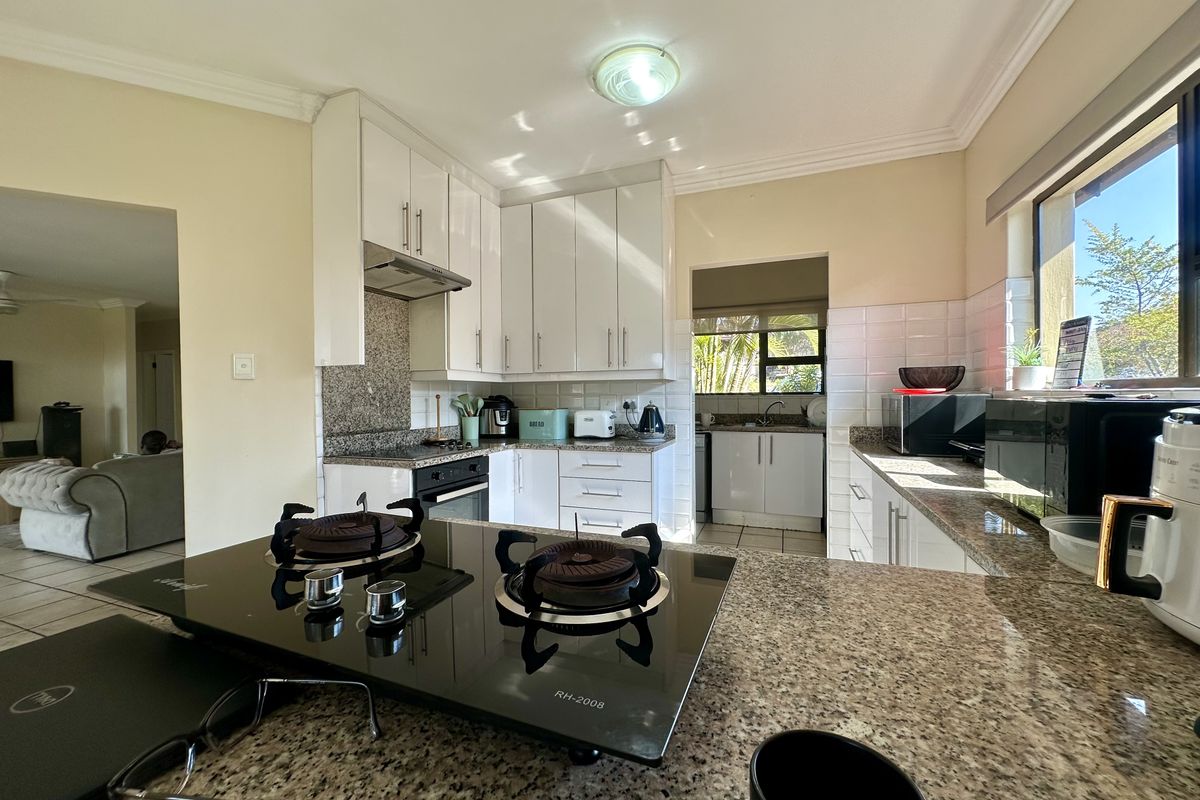 A functional kitchen featuring granite countertops, white cabinetry, a subway tile backsplash, and a built-in gas hob, with an adjacent scullery area.