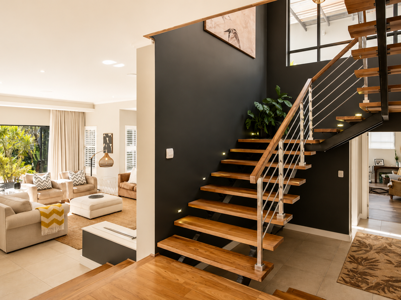 Modern entrance hall featuring a striking timber staircase with stainless steel balustrade, recessed lighting, and open-plan access to the living area.