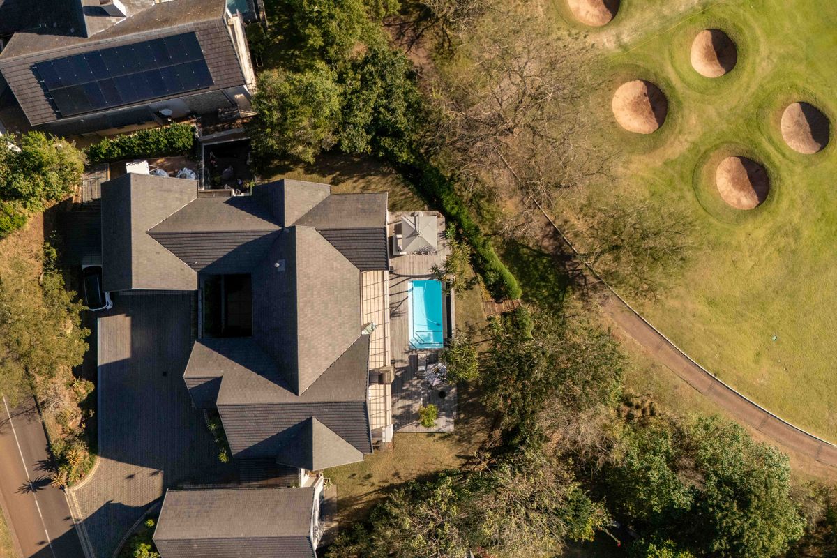 Aerial view of the property showcasing the roof structure, swimming pool, decking, and proximity to the adjacent golf course.