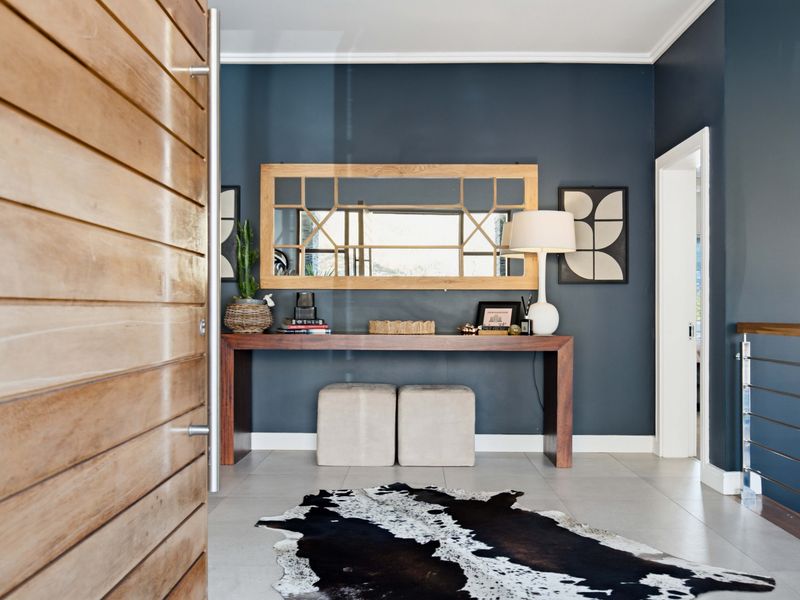 A welcoming entrance hall featuring a large timber pivot door, modern tiled flooring, and a stylish dark feature wall.