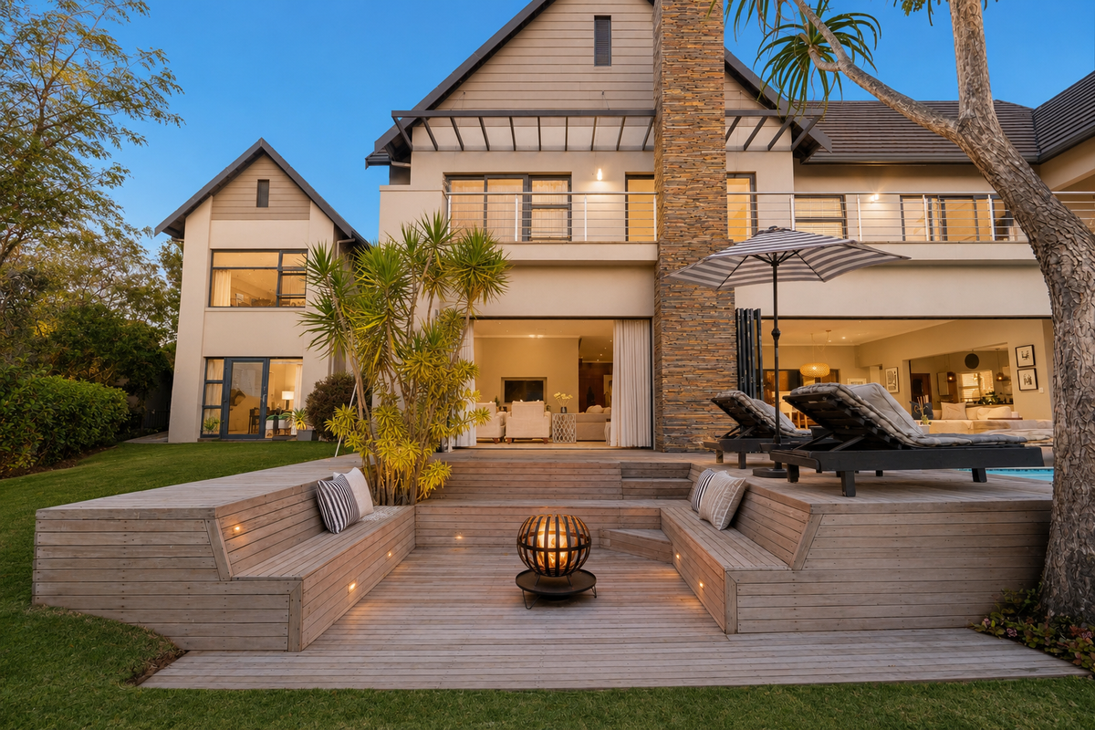 A beautifully landscaped rear exterior featuring a multi-level timber deck with built-in seating, a stone-clad chimney, and seamless indoor-outdoor flow through large sliding doors.