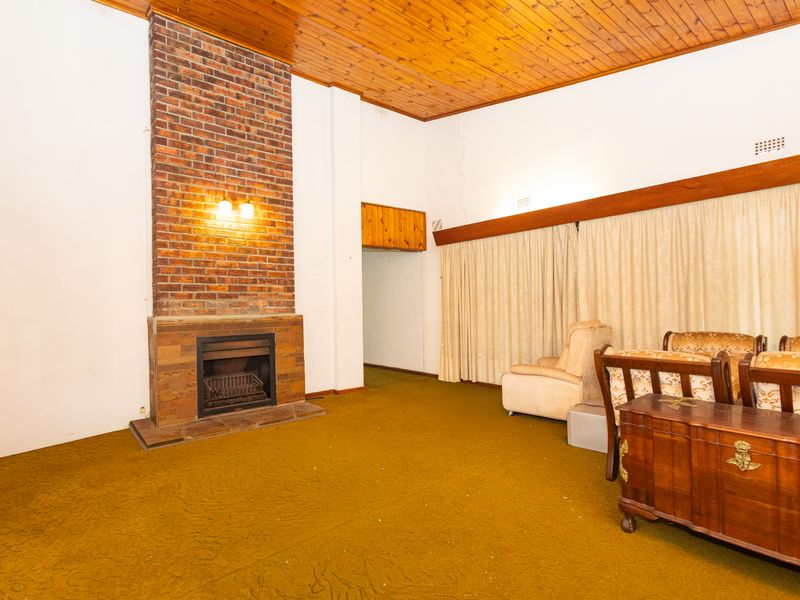 Spacious living room featuring a prominent brick fireplace and timber-paneled ceiling, offering a dated aesthetic ready for modernization.