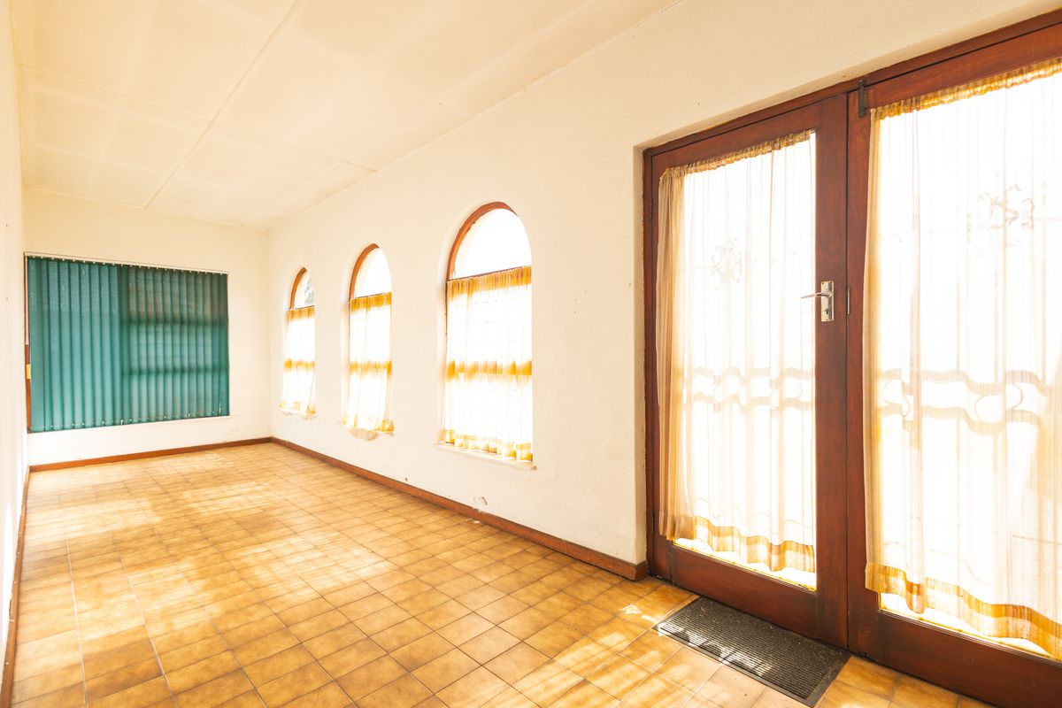 A bright, empty living area featuring tiled flooring, distinctive arched windows, and timber-framed glass doors providing access to the exterior.