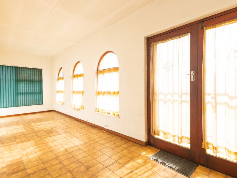 A bright, empty living area featuring tiled flooring, distinctive arched windows, and timber-framed glass doors providing access to the exterior.