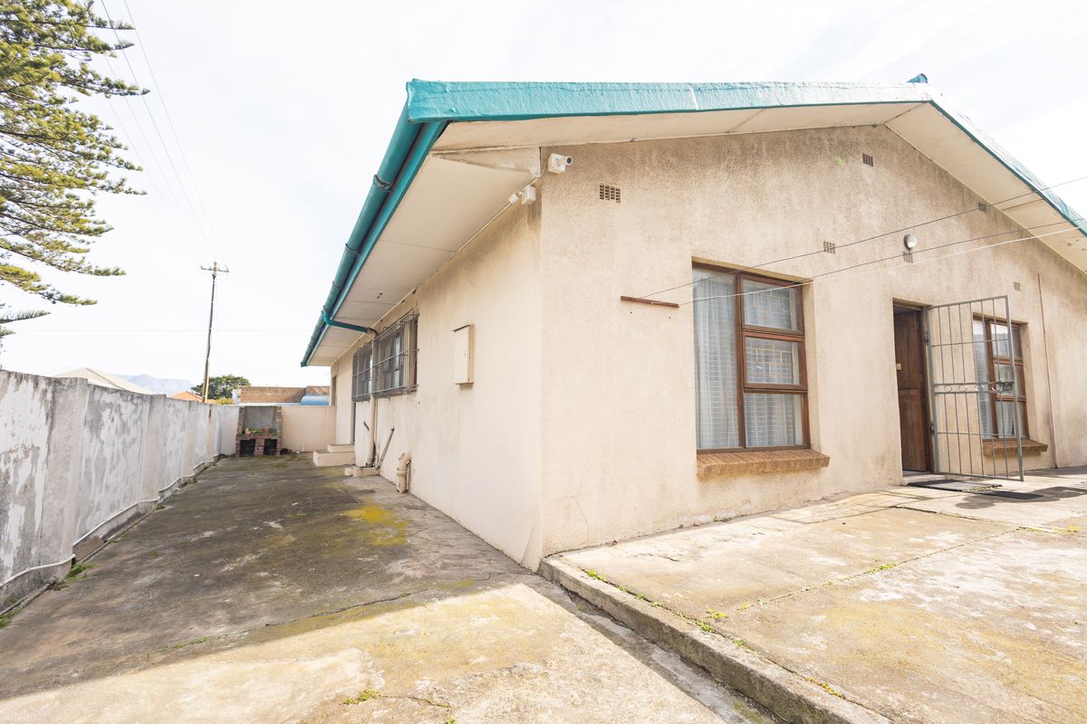 Rear exterior view of the house featuring a concrete paved area, a built-in brick braai, and security gates on the windows and doors.