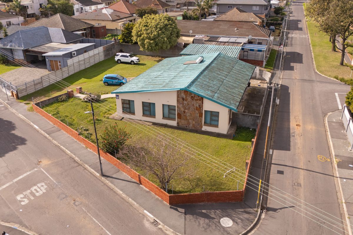 Aerial view of a corner property featuring a metal roof, stone facade detailing, and a surrounding brick boundary wall.