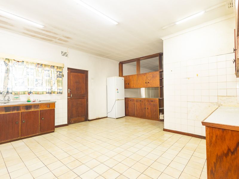 A dated kitchen featuring original wooden cabinetry, tiled flooring, and a stainless steel sink, offering significant potential for a modern renovation.