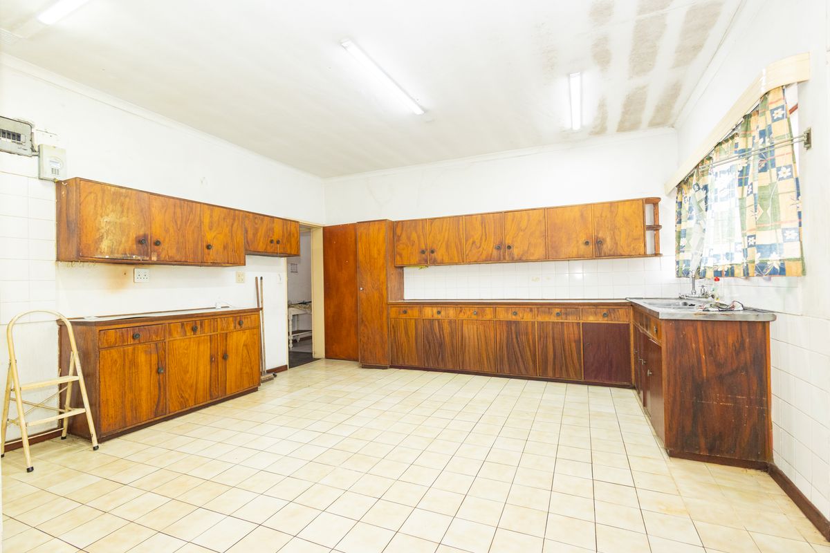 Spacious kitchen featuring extensive wooden cabinetry, tiled flooring, and a stainless steel sink, offering a functional layout ready for modernization.