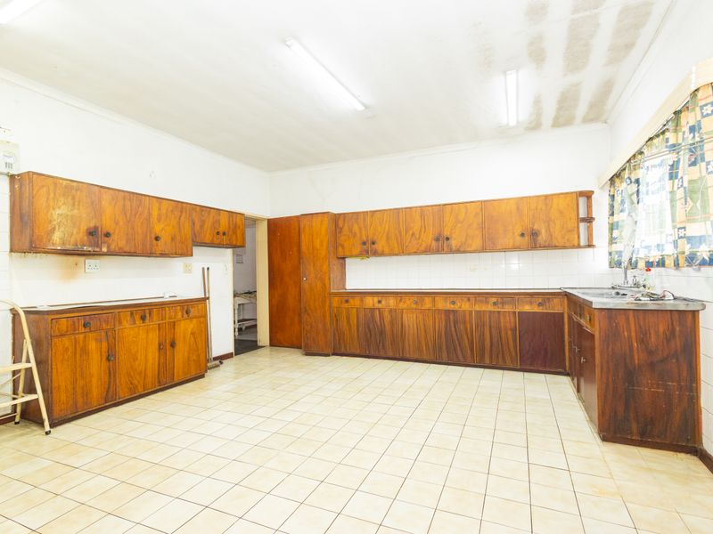 Spacious kitchen featuring extensive wooden cabinetry, tiled flooring, and a stainless steel sink, offering a functional layout ready for modernization.