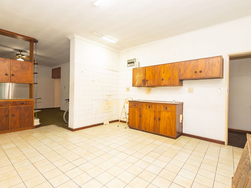 A dated kitchen space featuring original wooden cabinetry, tiled flooring, and wall tiling, offering significant potential for a modern renovation and layout update.