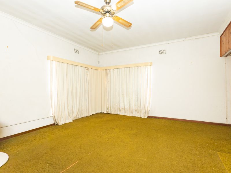 An empty living room featuring a ceiling fan, built-in storage, and dated carpet flooring, offering a blank canvas for renovation and modernization.