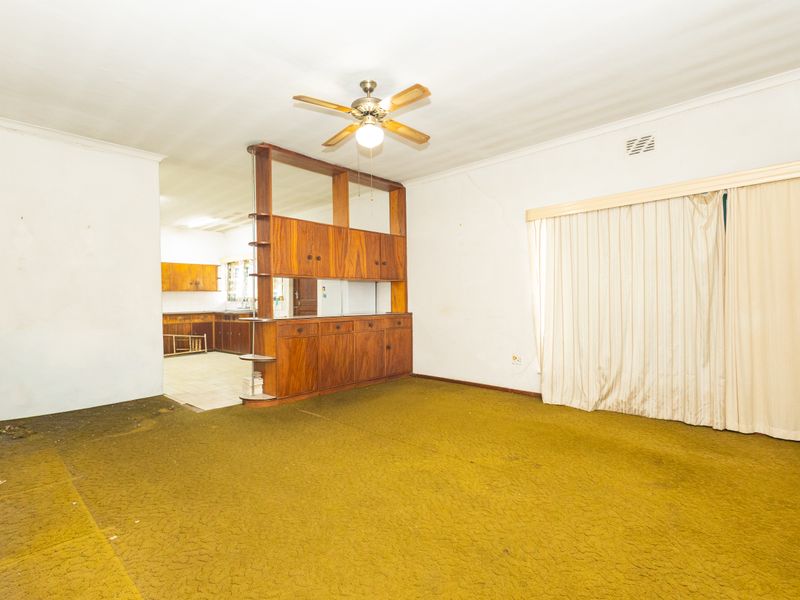 Open plan living area featuring a built-in wooden room divider, ceiling fan, and dated carpet flooring, offering significant potential for renovation and modernization.