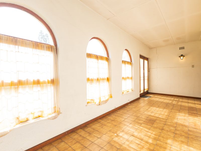 An empty living area featuring arched windows, tiled flooring, and natural light, requiring minor cosmetic repairs to the walls.