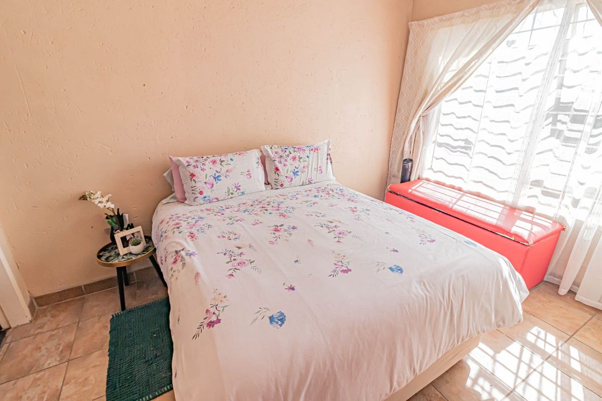 A functional bedroom featuring tiled flooring and a large window with security bars, providing natural light to the space.
