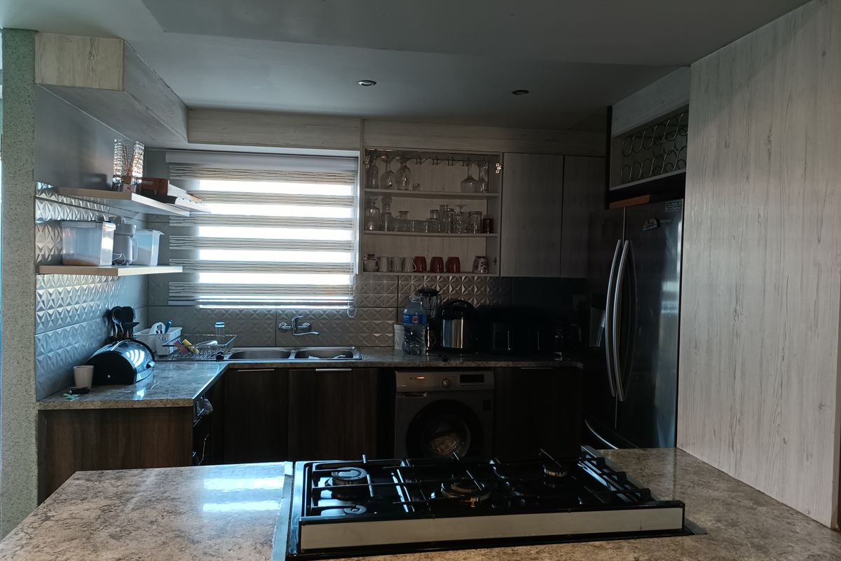 A functional kitchen featuring stone countertops, a built-in gas hob, integrated washing machine, and ample cabinetry with a modern tiled backsplash.