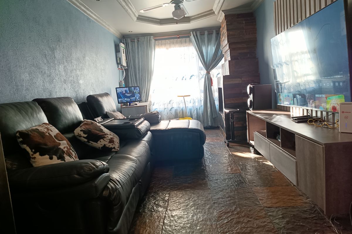 A living room featuring slate tile flooring, a stone fireplace, and a coved ceiling with a central fan.