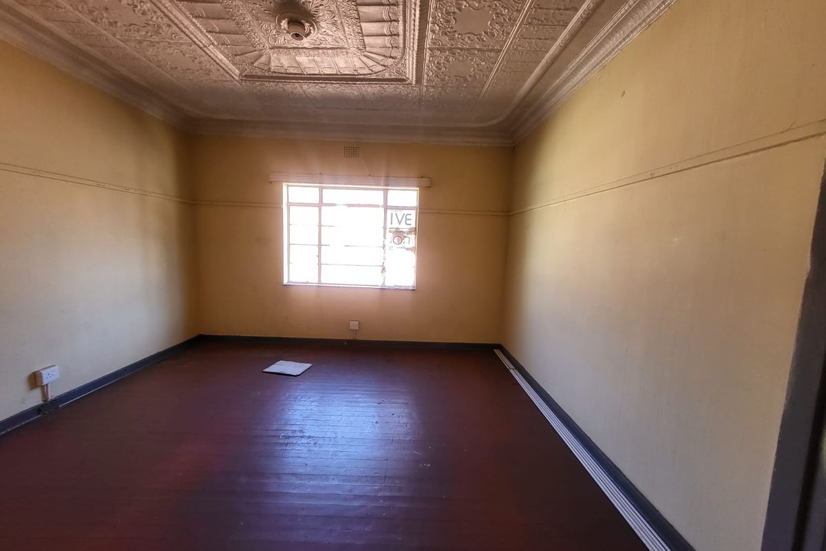 An empty bedroom featuring original ornate pressed metal ceilings, timber flooring, and a classic steel-framed window, offering a blank canvas for renovation.