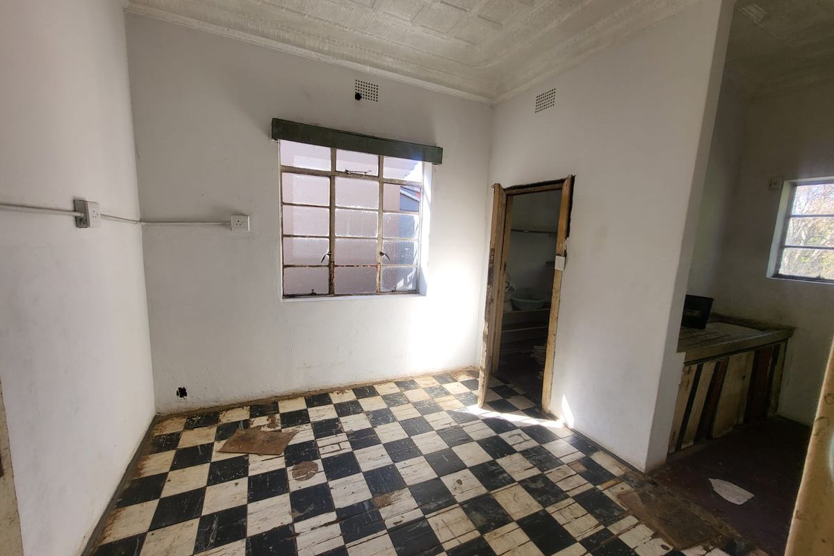 An empty kitchen space featuring original checkerboard floor tiles, a pressed metal ceiling, and a steel-framed window, requiring significant renovation and cosmetic updates.