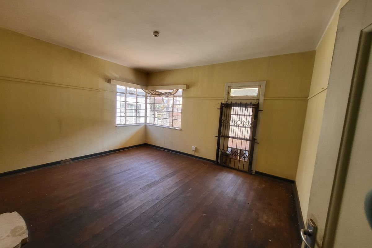 An empty living room featuring original timber flooring, steel-framed windows, and a security gate, offering a blank canvas for renovation.