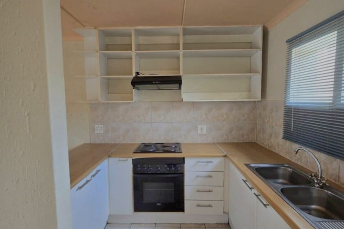 A functional kitchen featuring built-in oven, electric hob, extractor fan, double bowl sink, and open shelving with laminate countertops and tiled backsplash.