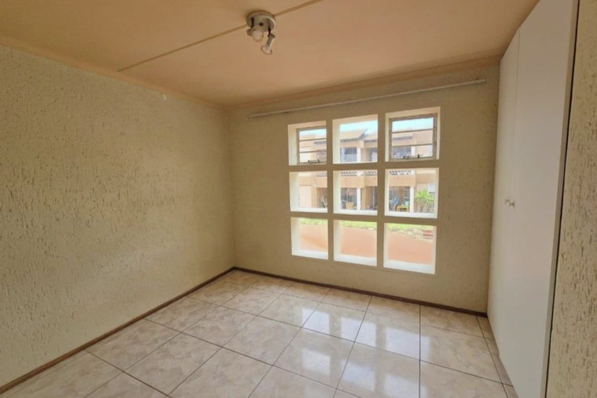 An empty bedroom featuring tiled flooring, built-in cupboards, and a grid-style window, offering a blank canvas for renovation or restyling.