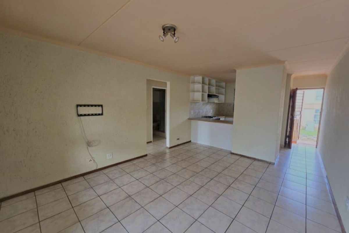 An open-plan living and kitchen area featuring tiled flooring, built-in cabinetry, and a functional kitchen layout, presenting a blank canvas for renovation.