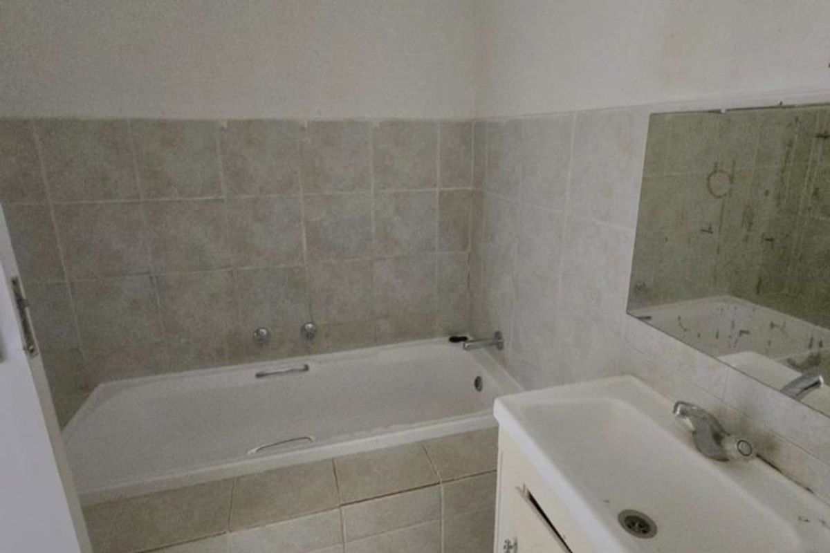 A dated bathroom featuring a built-in bathtub with tiled surround, a vanity cabinet with basin, and a wall-mounted mirror.